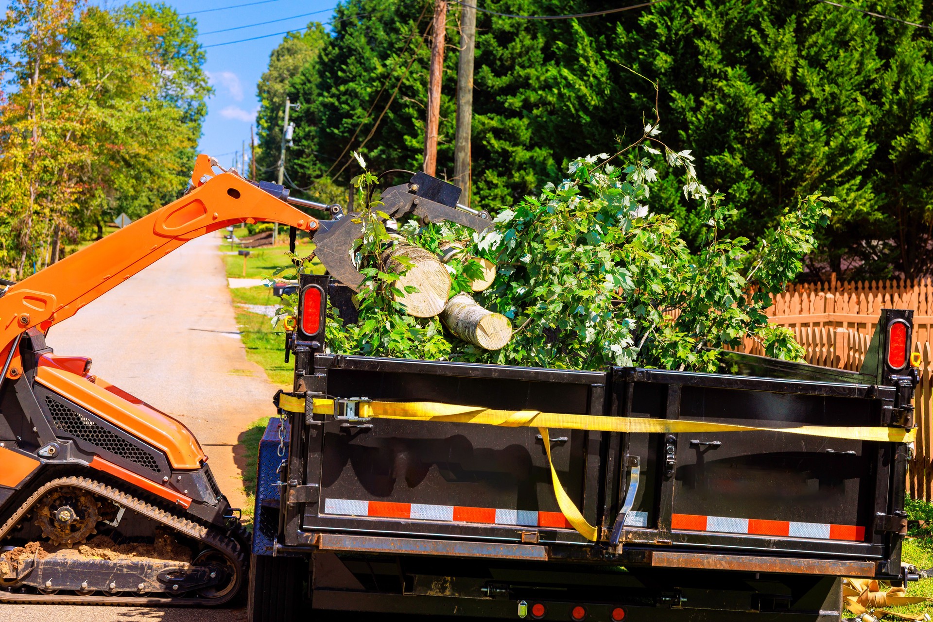 Heavy equipment crawler loader clears fallen branches from residential street in summer