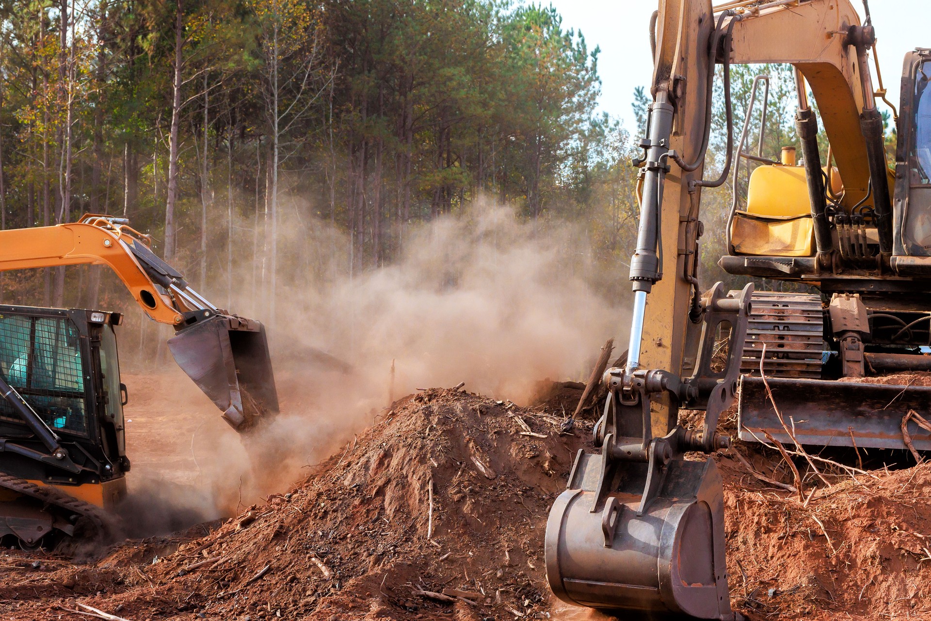 Heavy machinery clears land in forested area to prepare for construction project during daytime
